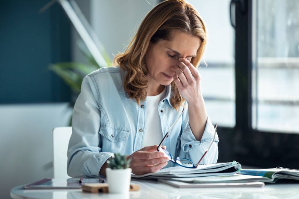 Bild på en utmattad kvinna med huvudvärk som arbetar med sin laptop.