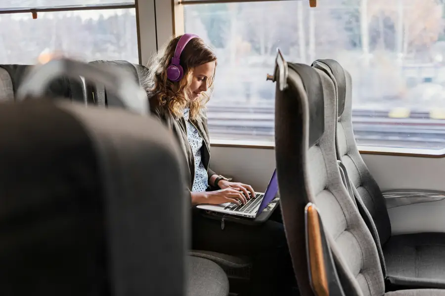 Kvinna på tåg sitter och skriver på sin laptop, dator.