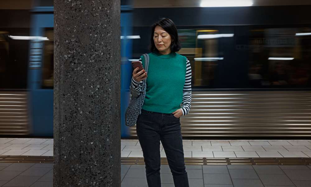 Kvinna som står och kollar på sin mobil på en tunnelbaneperrong.