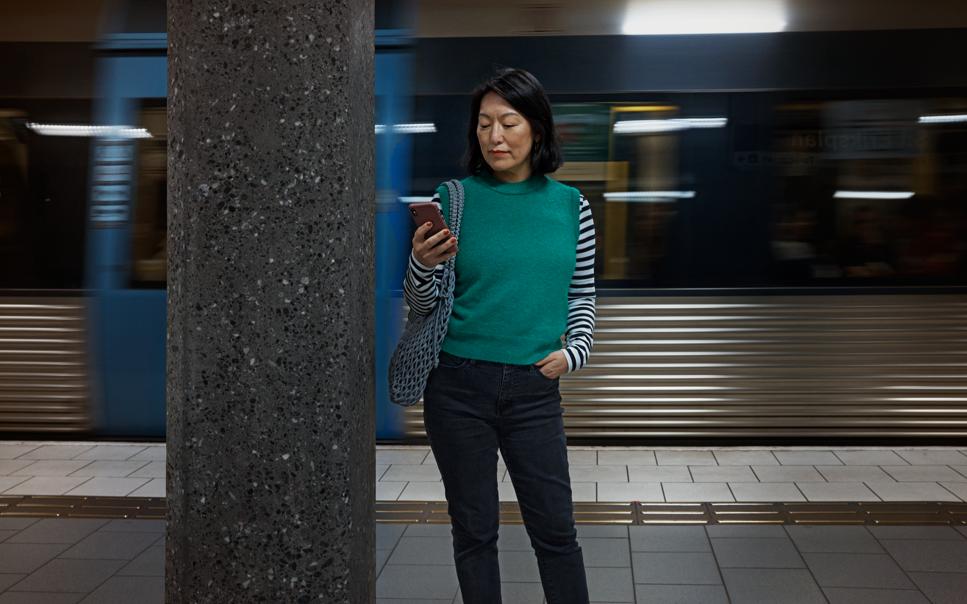 Kvinna som står och kollar på sin mobil på en tunnelbaneperrong.