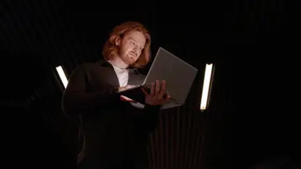 Man som håller och tittar i en laptop i ett mörkt rum.
