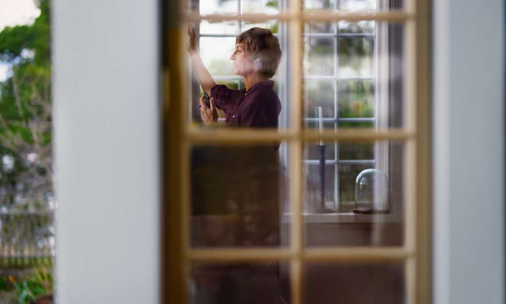 Kvinna med mobil och hörlurar i villa syns genom fönster