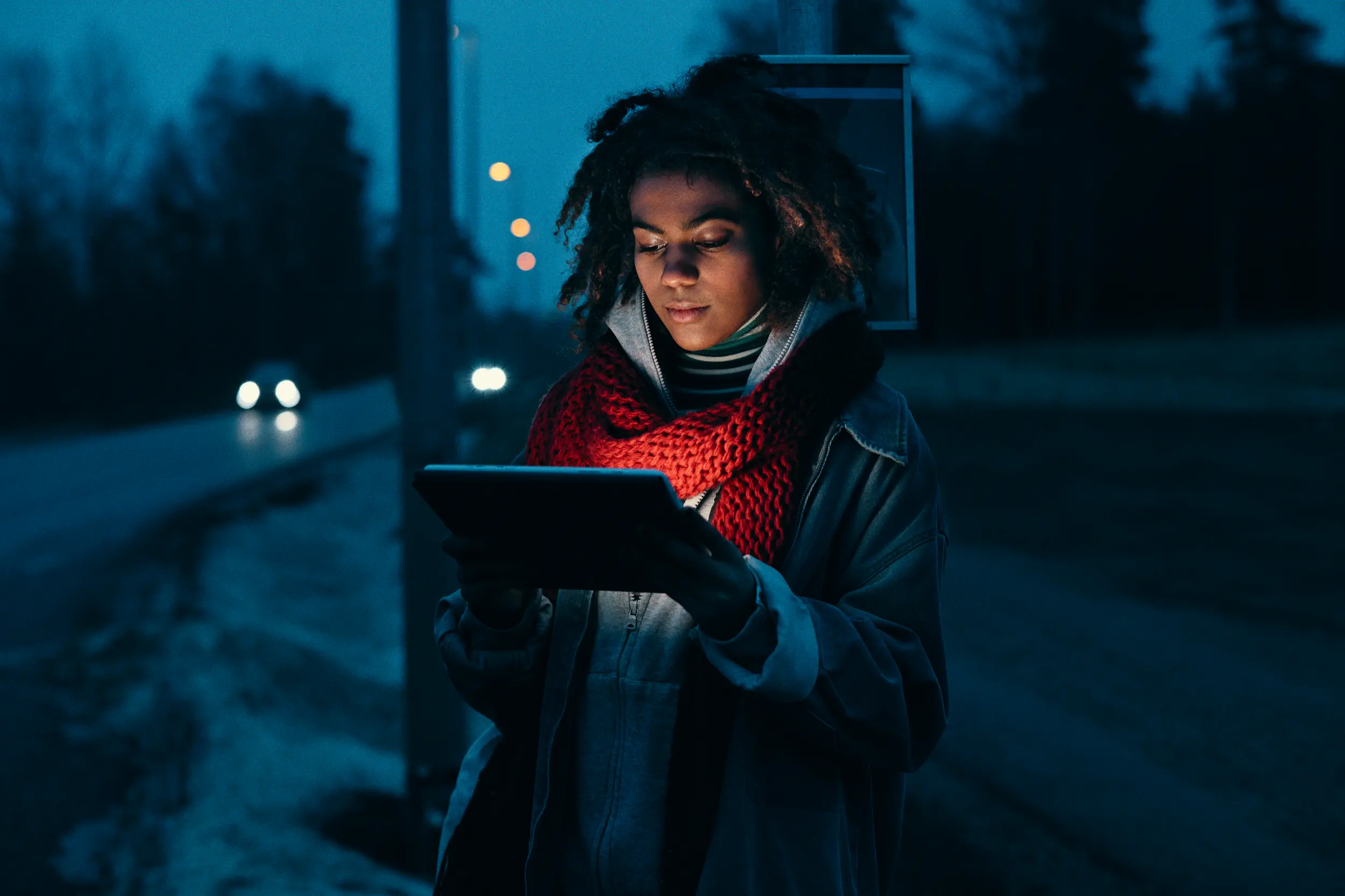 Kvinna står vid busstation på kvällen med surfplatta