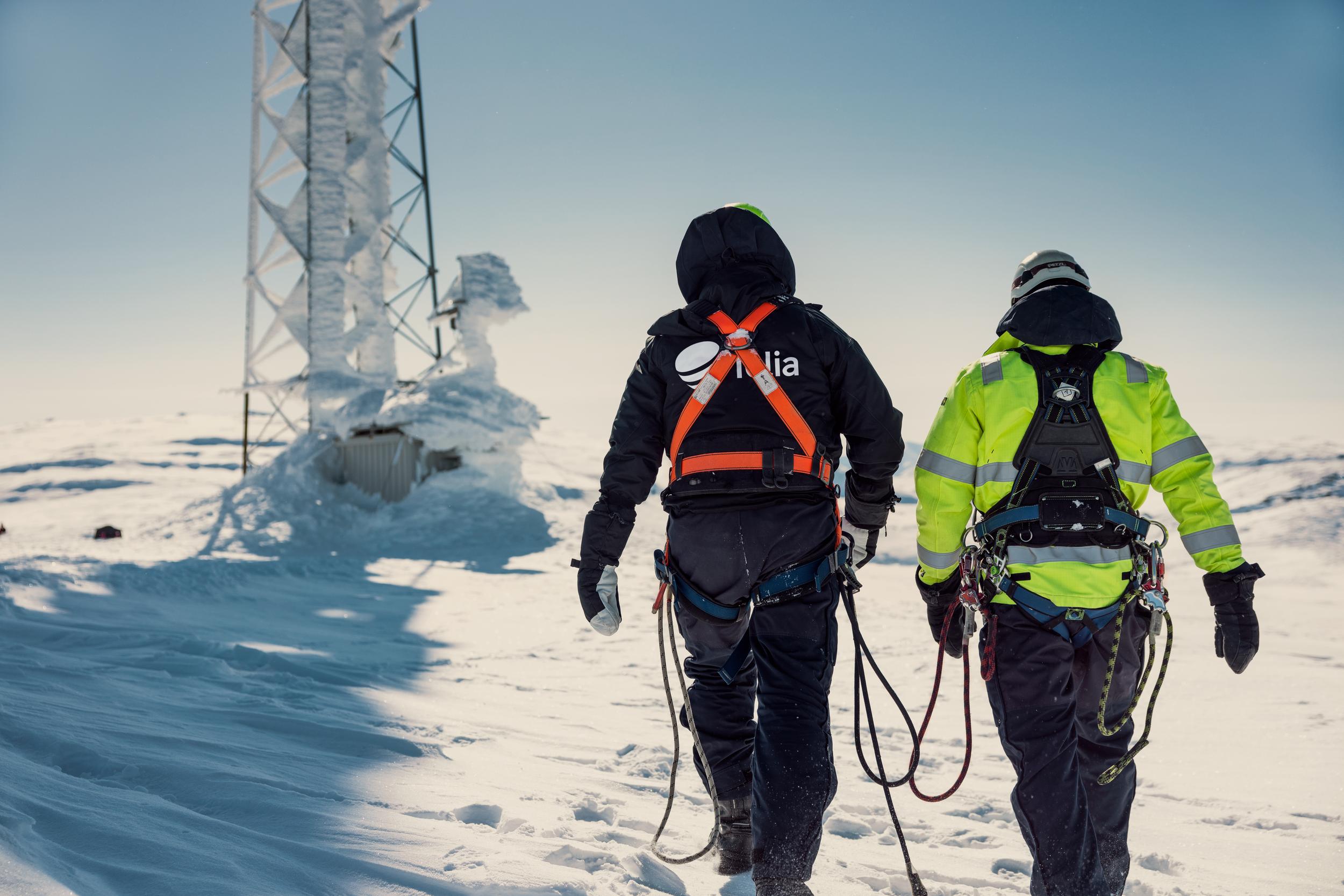 Arbetare i snöigt landskap framför mobilmast.