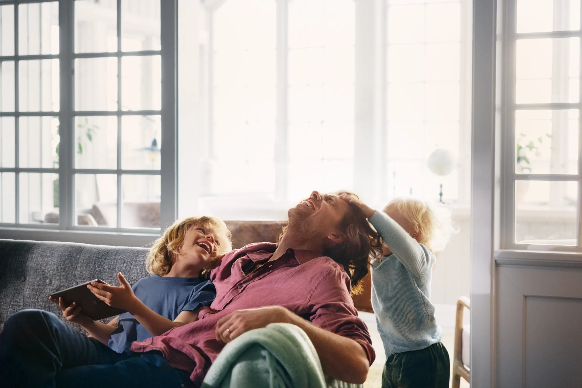 Pappa och två barn skrattar med surfplatta