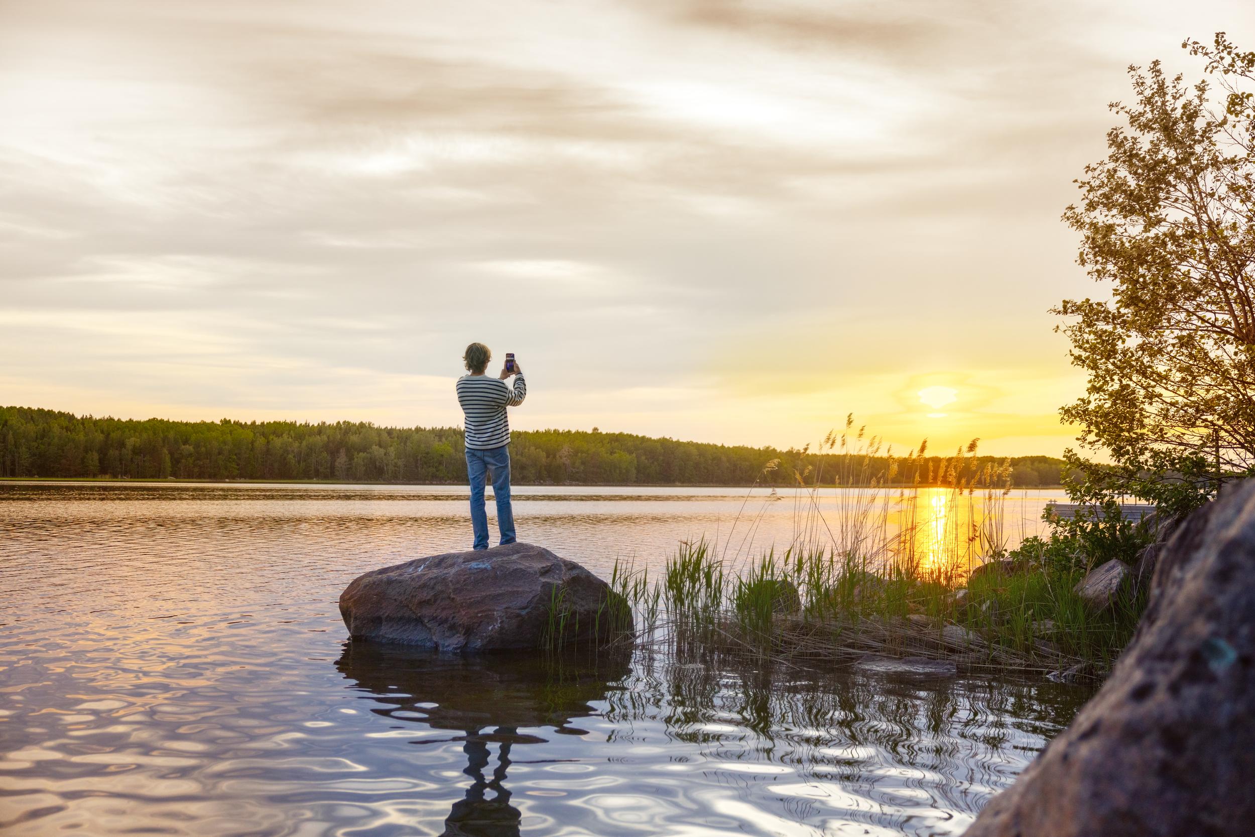 Kvinna som står på en liten holme och fotograferar solnedgången