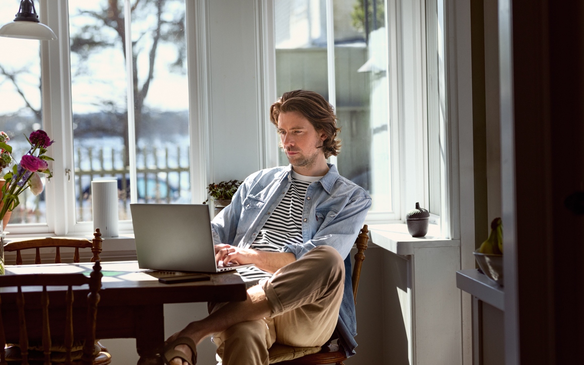 Man i tofflor sitter framför laptop och arbetar hemma.