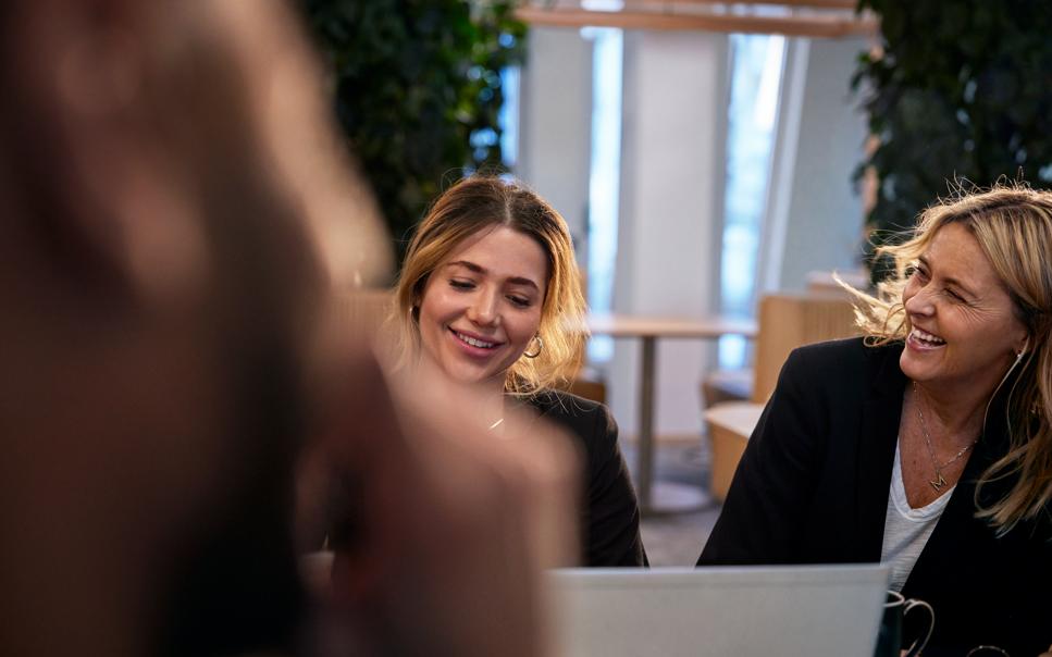 Två kvinnor skrattar vid laptop i kontorsmiljö