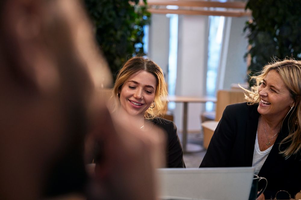 Två kvinnor skrattar vid laptop i kontorsmiljö