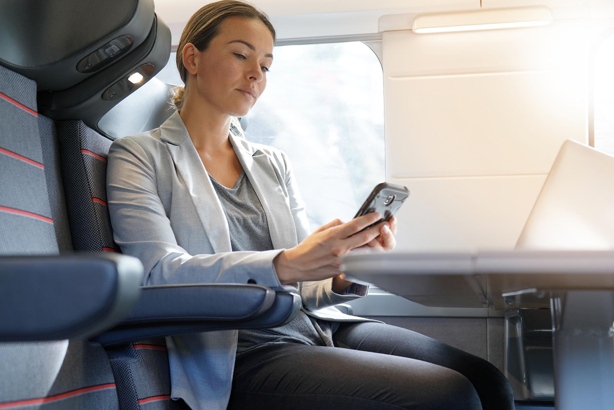 Kvinna på affärsresa på tåg, tittar på mobil och har laptop framför sig.