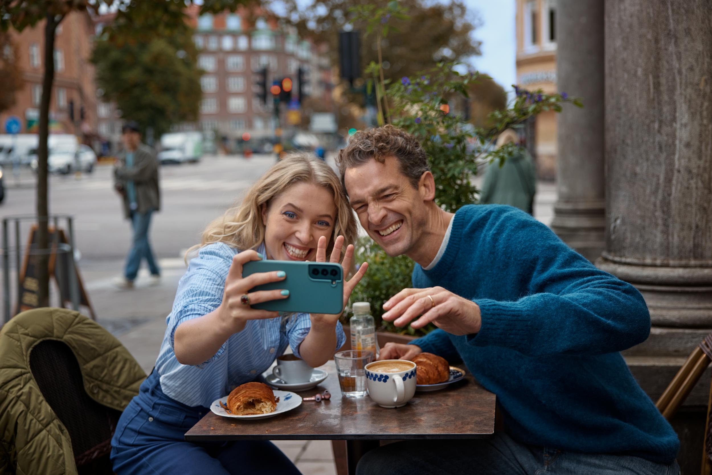 Kvinna och man sitter på en uteservering och tar en selfie tillsammans och ler