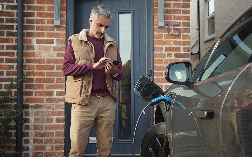 Man texting while charging electric car outside a house.