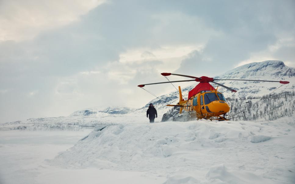 Person i vinterlandskap går bredvid helikopter.