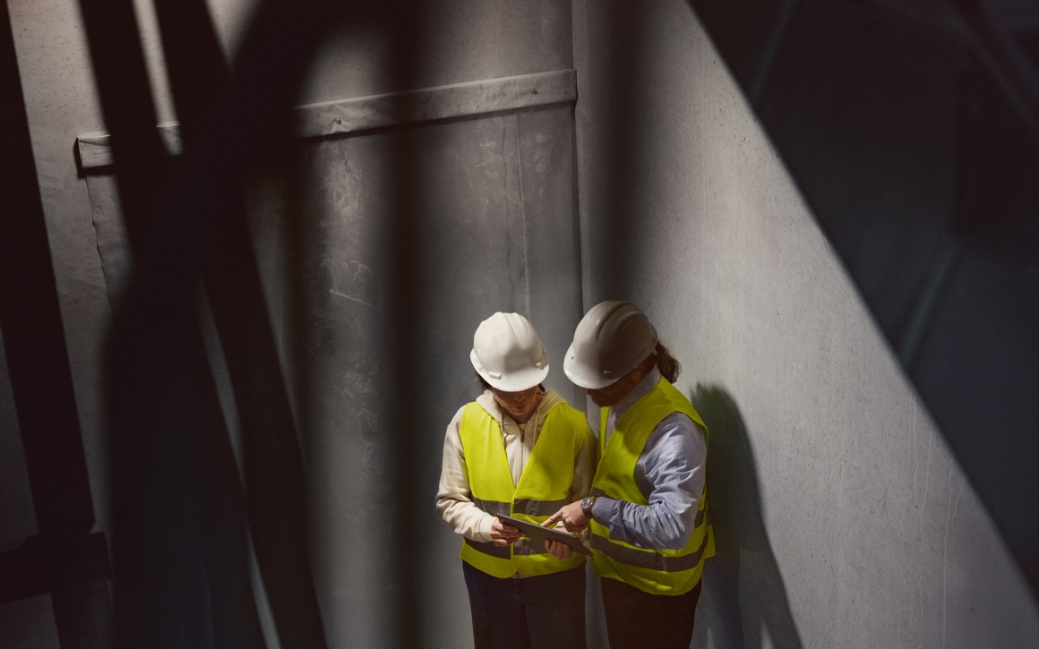 Två personer i varselkläder som tittar på en platta