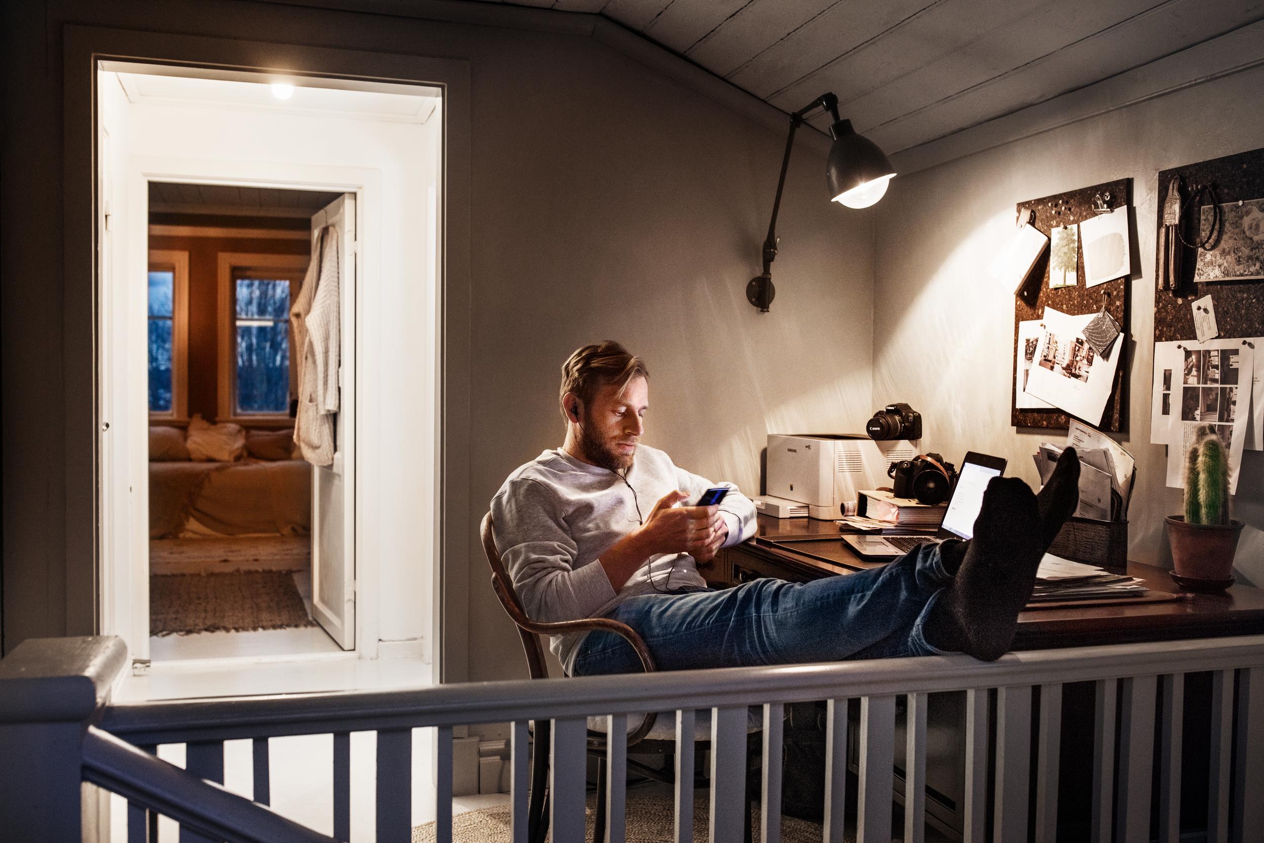 En man sitter med sin mobil vid skrivbordet hemma.