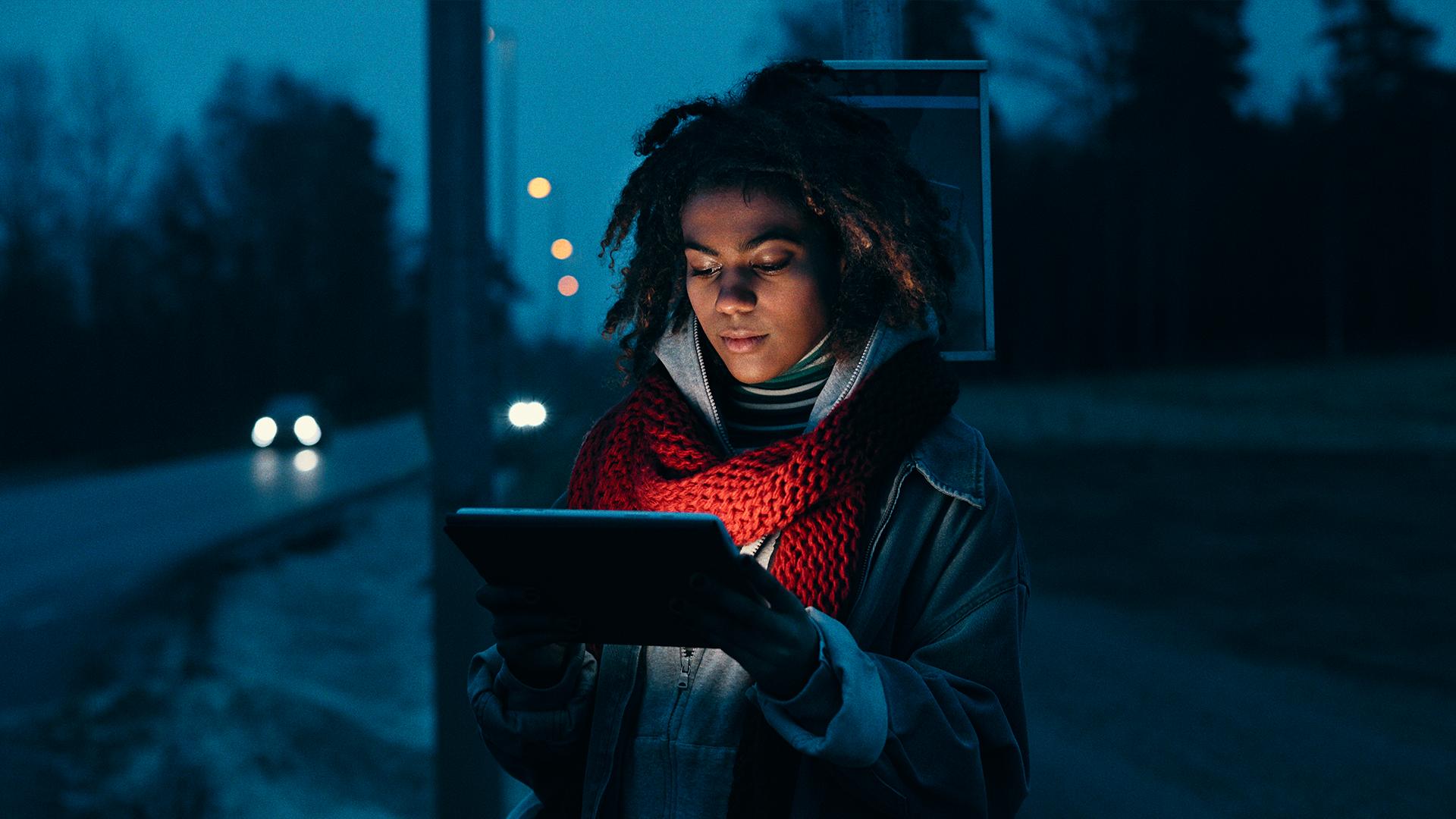 Kvinna på busshållsplats tittar på en surfplatta