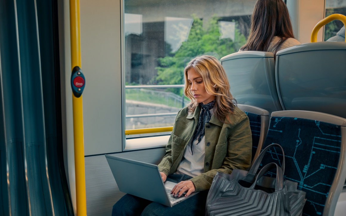 En kvinna som sitter på tvärbanan och surfar på sin laptop.