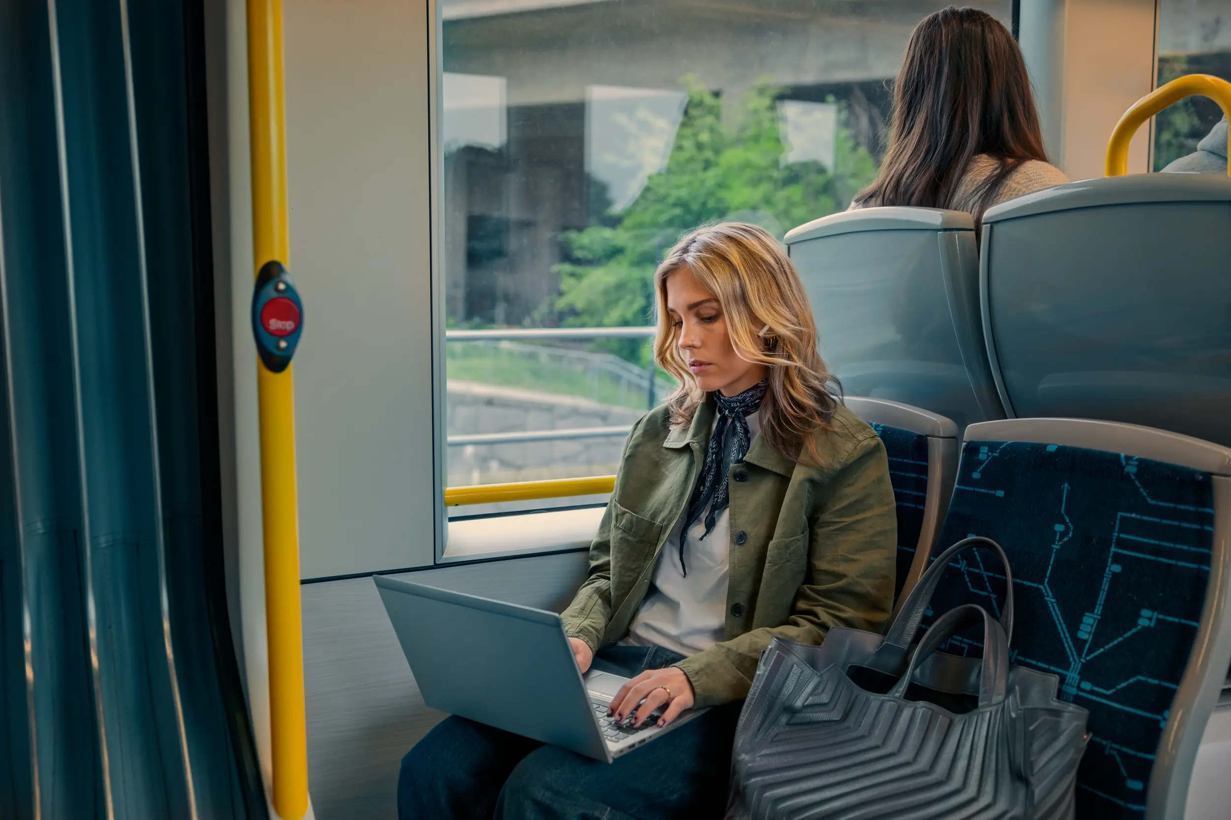 En kvinna som sitter på tvärbanan och surfar på sin laptop.