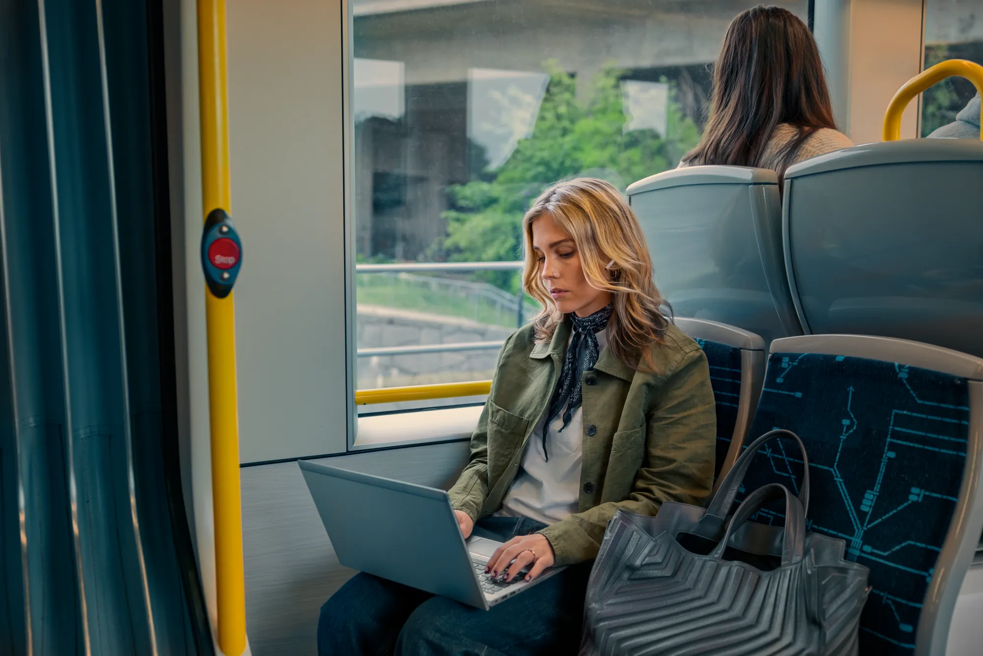 En kvinna som sitter på tvärbanan och surfar på sin laptop.