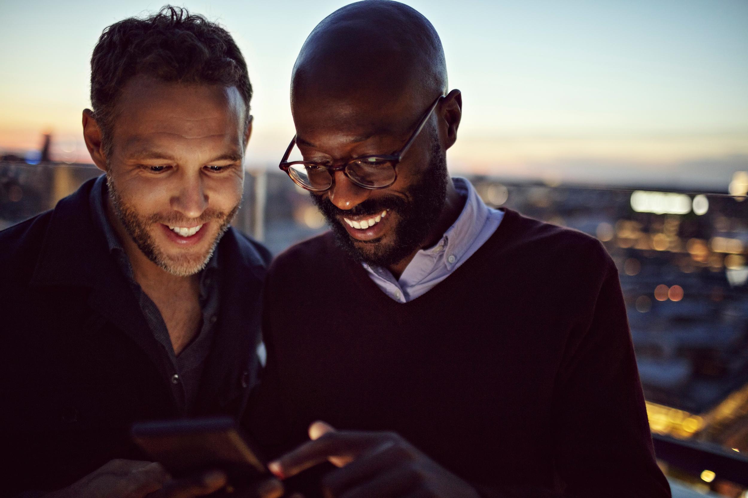 Två män utomhus som tittar på en upplyst mobiltelefonskärm.