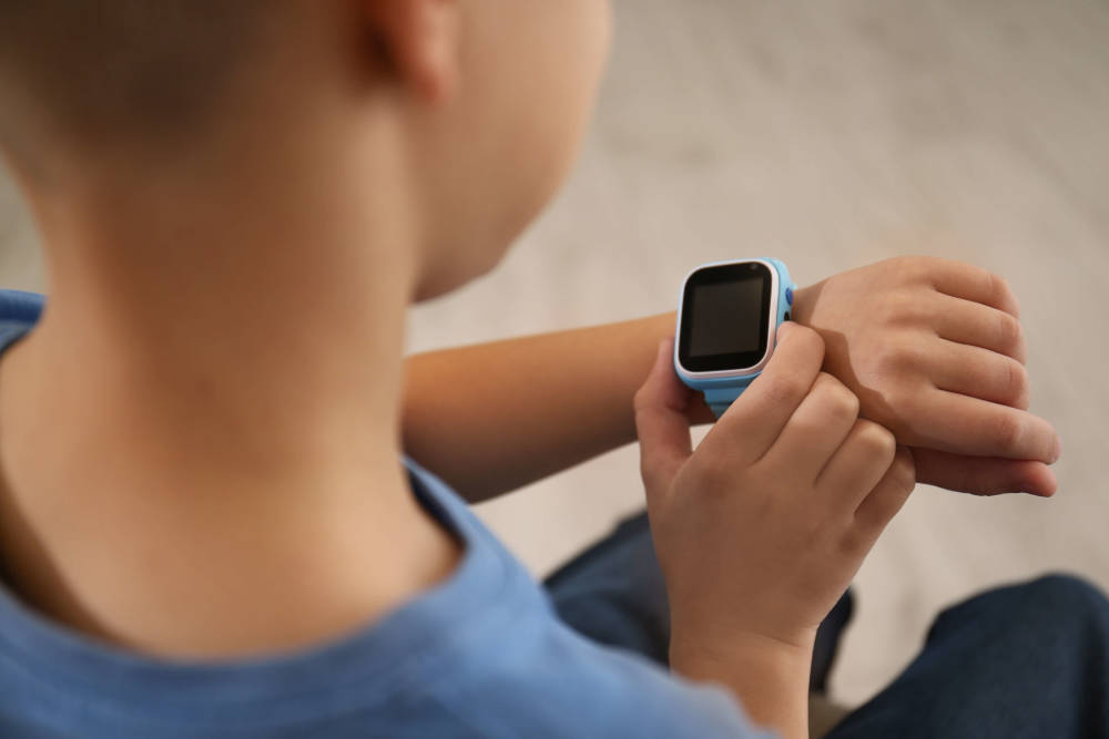 En pojke som tittar och klickar på sin blåa smartklocka från Xplora som han har på armen runt handleden.
